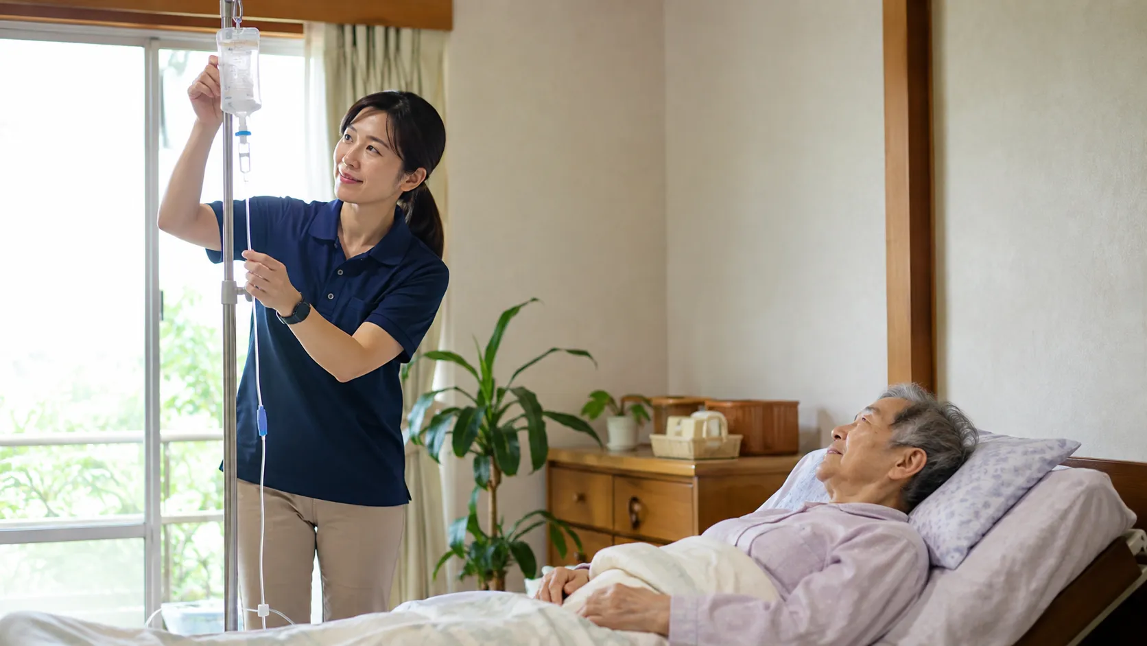 自宅の寝室で点滴を確認する看護師と利用者